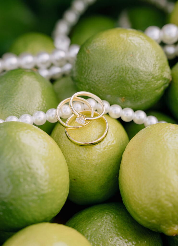 Verlobungsring und Eheringe als Detailaufnahme auf grünen Limetten mit Perlenkette bei einer modernen Hochzeit