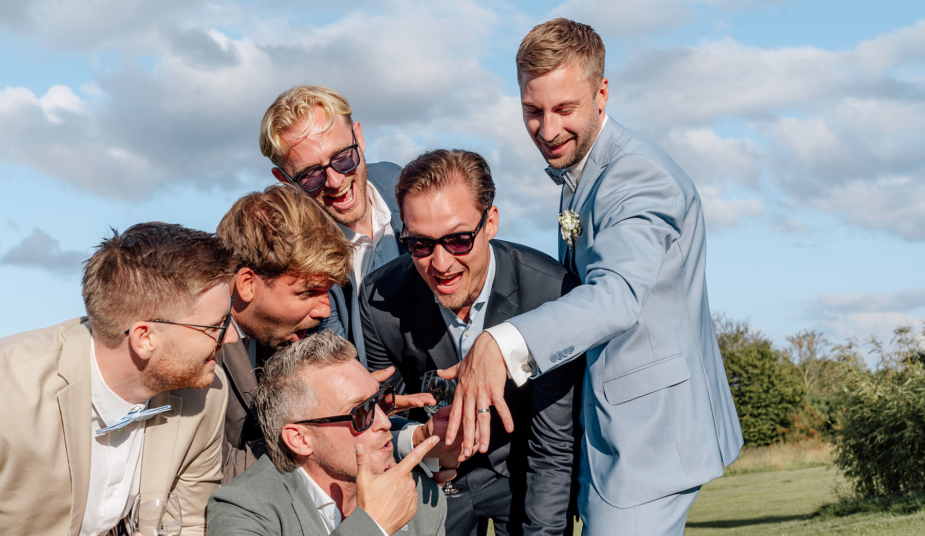 Freunde des Bräutigams bestaunen den Verlobungsring bei einem emotionalen Heiratsantrag von der Frau an den Mann im Freien